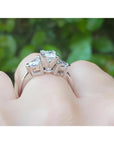 14K white gold ring with a princess cut diamond center and trillion side diamonds, worn on a finger.