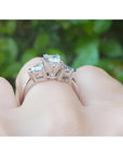 14K white gold ring with a princess cut diamond center and trillion side diamonds, worn on a finger.
