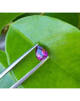Natural loose ruby pear shaped, front side gemstone held by tweezers on a green leaf
