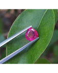 1.19 carat pear cut natural ruby gemstone, sparkling medium deep red, held by tweezers over a green leaf.