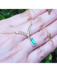 14K yellow gold necklace with a baguette-cut Colombian emerald dangling from a diamond-studded curved V.