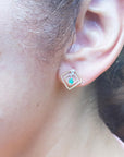 An ear wearing an earring of 14K yellow gold emerald post earring with round cut Colombian emerald.