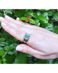 Hand wearing a men's emerald bezel set ring yellow 14k gold with a green leafy background.