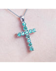 White gold emerald cross necklace on a light pink skin background.