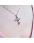 A 18k white gold emerald cross pendant necklace on a person's neck.