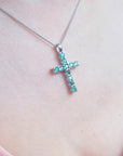 A 18k white gold emerald cross pendant necklace on a person's neck.