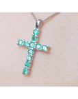 Cross-shaped Muzo emeralds cross pendant on a chain against a light skin background.