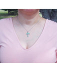 A woman wearing a pink top with a natural emerald cross necklace pendant.