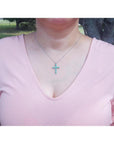Woman wearing an 18K white gold cross pendant necklace with eleven round-cut Colombian emeralds.