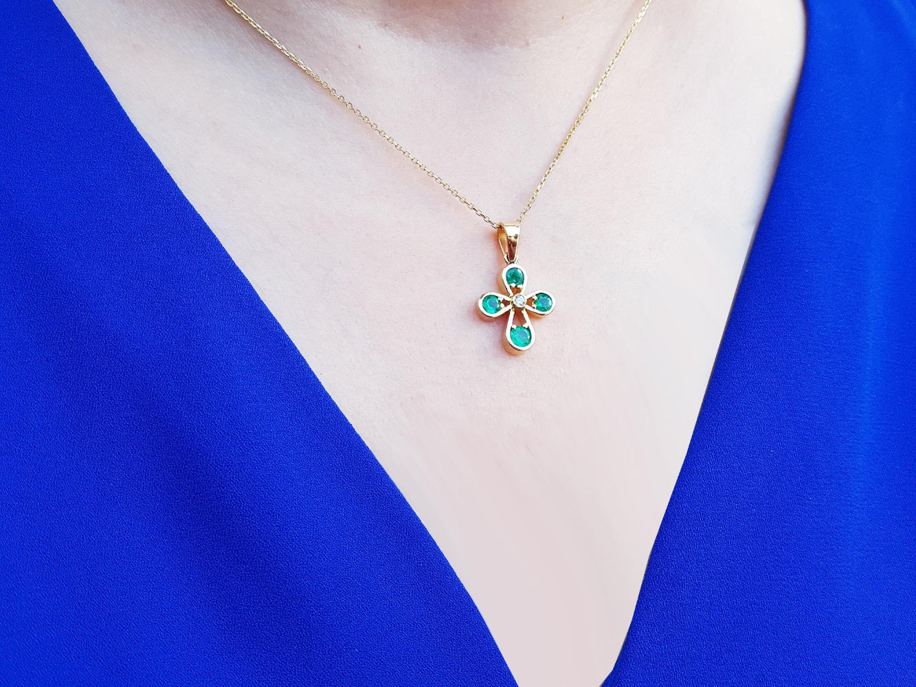Necklace with a floral natural emerald cross pendant on a blue garment.