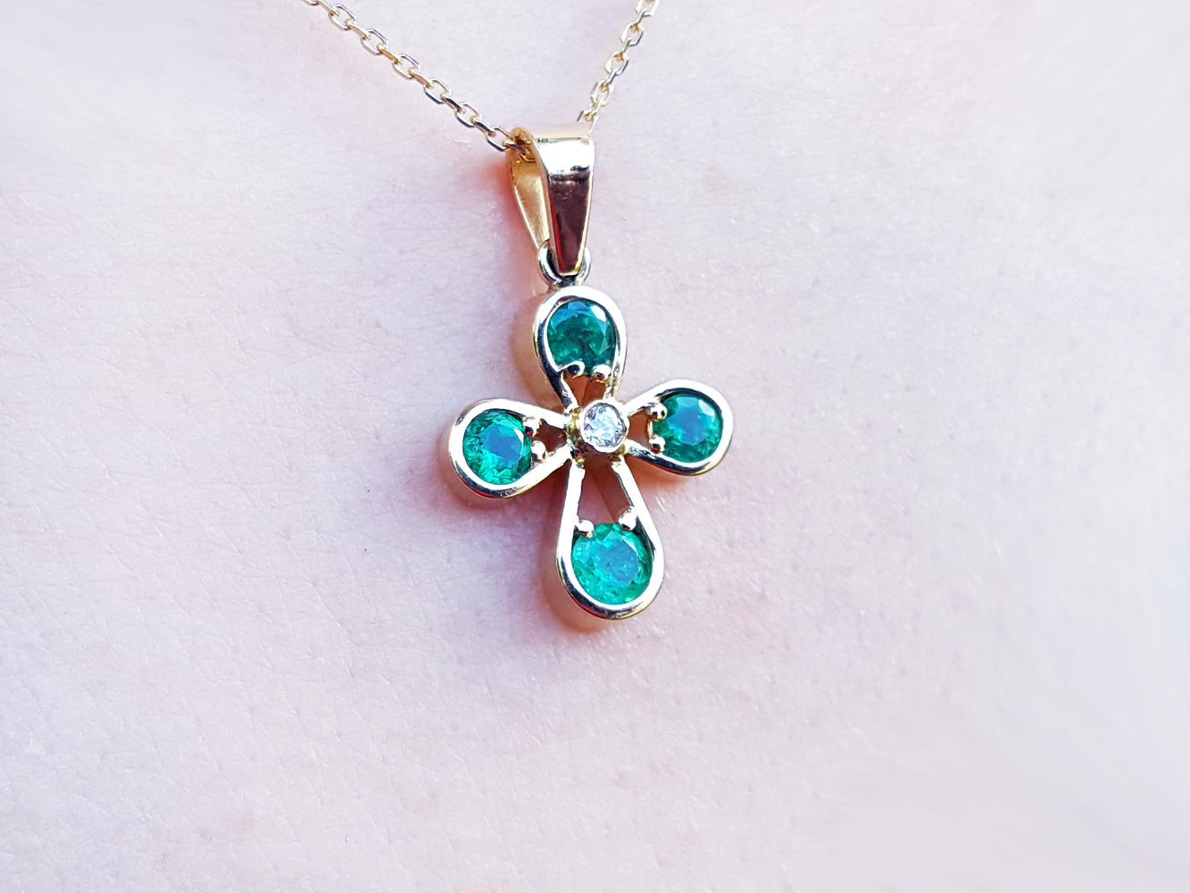 Muzo emerald cross pendant necklace on a light pink skin background.