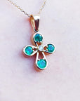 Muzo emerald cross pendant necklace on a light pink skin background.