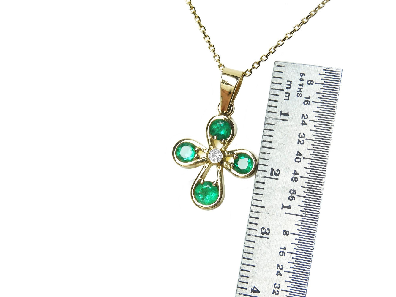 Gold necklace with an emerald cross pendant next to a ruler for scale on a white background.