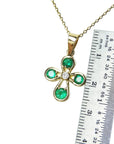 Gold necklace with an emerald cross pendant next to a ruler for scale on a white background.