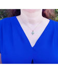 Yellow gold cross pendant with round-cut emeralds on a woman's neck, wearing a blue top.