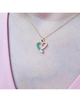 18K yellow gold heart pendant with natural emeralds and a diamond, worn on a woman's neck.