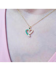 18K yellow gold heart pendant with natural emeralds and a diamond, worn on a woman's neck.