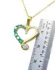 Gold heart-shaped pendant with emeralds and diamonds on a gold chain, next to a ruler for scale.