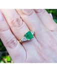 18K yellow gold ring with a GIA certified emerald and side trillion diamonds on a hand.