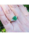 18K yellow gold ring with a GIA certified emerald and side trillion diamonds on a hand.