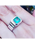 Men's 18K white gold ring with a bezel-set, deep bluish-green Muzo Colombian emerald.