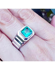Men's 18K white gold ring with a bezel-set, deep bluish-green Muzo Colombian emerald.