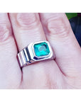 A 18k white gold men's ring with a bezel set natural colombian emerald worn on a finger.