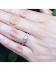 14K white gold engagement ring with a round center diamond and trillion side diamonds on a hand.