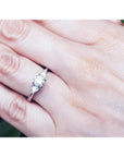 14K white gold engagement ring with a round center diamond and two trillion side diamonds on a hand.