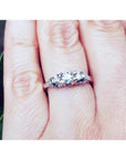 14K white gold three-stone round cut diamond engagement ring with pave accent diamonds on a hand.