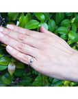 14k white gold engagement ring with a round central diamond and side baguette diamonds on a hand.