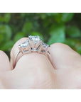 14K white gold ring with a princess cut diamond center and trillion side diamonds, worn on a finger.
