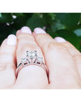 White gold 14K three-stone princess cut diamond ring on a hand, featuring a large center diamond.
