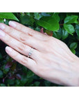White gold 14K princess cut three-stone diamond ring on a hand, surrounded by green leaves.