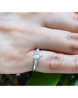 Heart-cut diamond engagement ring with side baguette diamonds in 14K white gold on a finger.