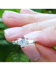 Heart-cut diamond ring with side baguette diamonds in 14K white gold, held by fingers.