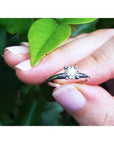 Round cut diamond solitaire engagement ring in 14K white gold, held by fingers with a green leaf.