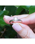 Hand holding a round cut diamond solitaire engagement ring in 14K white gold with an illusion setting.