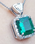 A natural certified emerald pendant with gold chain on a light background