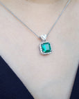 Emerald green gemstone necklace on a person wearing a dark blue top.