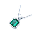Emerald cut Colombian emerald pendant in 18K white gold with diamond halo and bail.