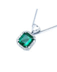 Emerald cut Colombian emerald pendant in 18K white gold with diamond halo and bail.
