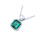 Emerald cut Colombian emerald pendant in 18K white gold with diamond halo and bail.