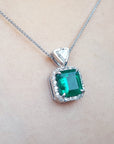Emerald natural gemstone pendant on a gold chain against a neutral background.