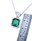 Emerald pendant on a white gold chain with a ruler for scale on a white background.