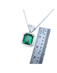 Emerald cut Colombian emerald pendant in 18K white gold with diamond halo, next to a ruler.