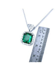 Emerald cut Colombian emerald pendant in 18K white gold with diamond halo, next to a ruler.
