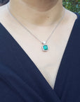 Person wearing a necklace with a colombian emerald pendant against a blurred natural background.