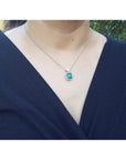 Person wearing a necklace with a colombian emerald pendant against a blurred natural background.