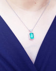 Person wearing a necklace with an emerald pendant against a dark blue background